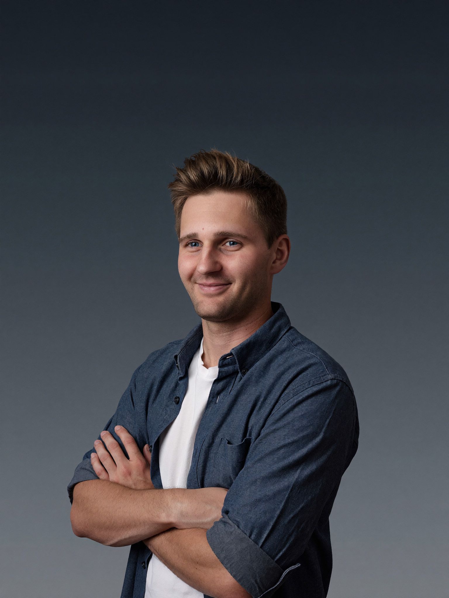 Kevin Baum im Jeanshemd mit verschränkten Armen vor dunklem Hintergrund.